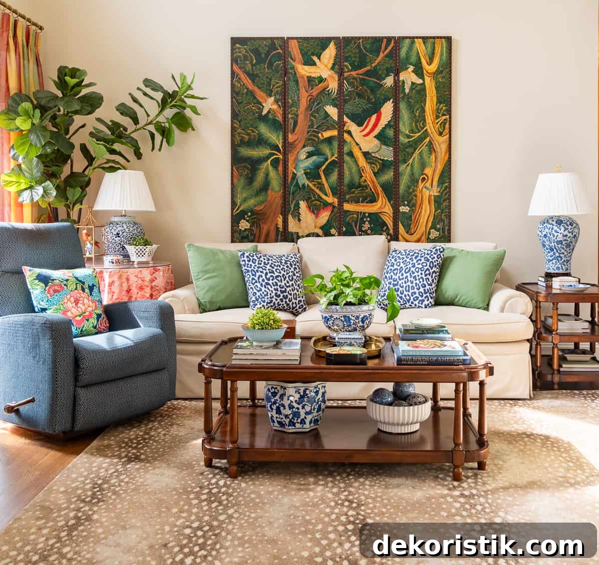 beige couch against the wall with a blue recliner beside it and colorful pillows on the couch and accessories on the tables
