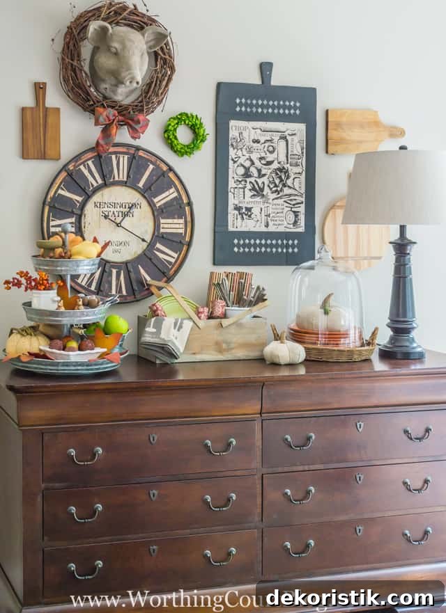 Fall decor above a kitchen sideboard with a cloche and a pumpkin under it, and a small wreath on the wall.