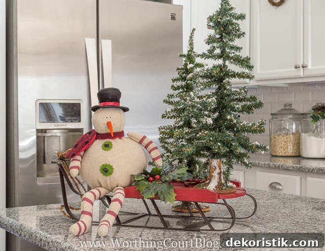 A snowman figurine is on a sleigh with mini trees.