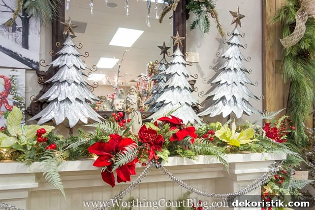 Decorative Christmas trees on the mantel plus red flowers and berries.