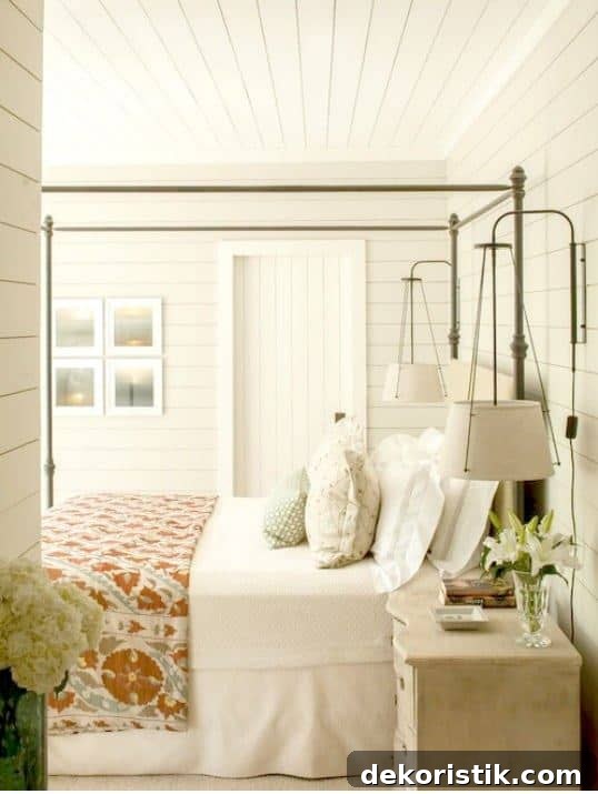 Bedroom with white walls and neutral bedding illuminated by layered lighting.