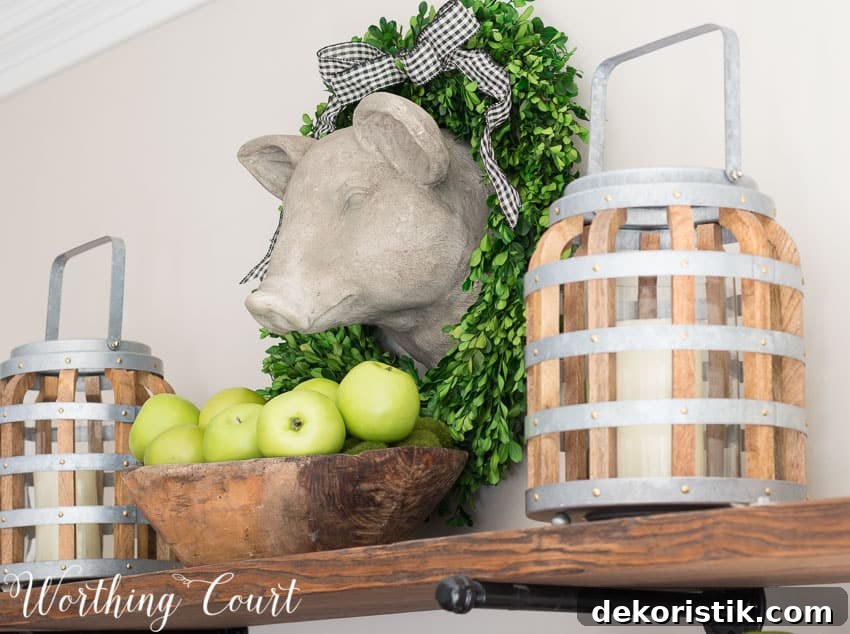 A faux pig head, surrounded by a preserved boxwood wreath, hangs above open rustic farmhouse kitchen shelves