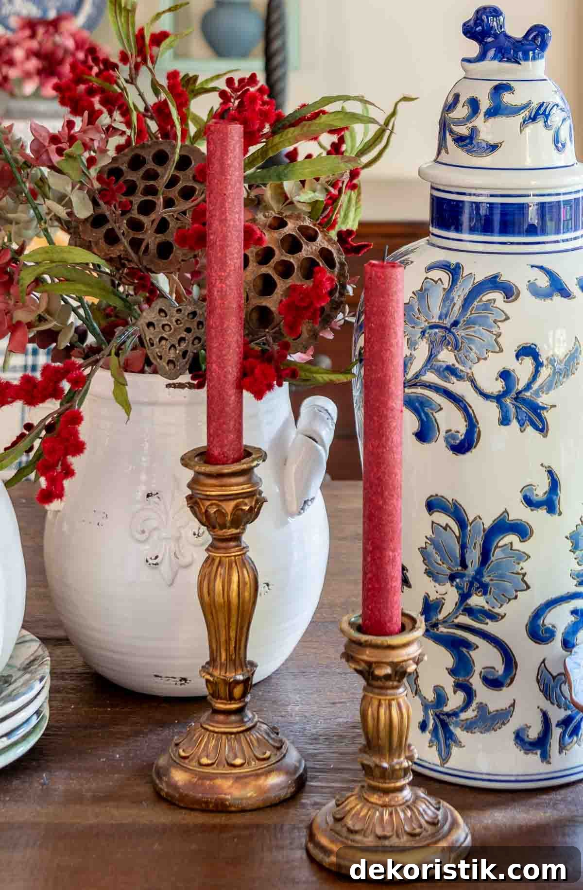 a diy fall table centerpiece using blue, white and burgundy colors, consisting of a large lidded urn, a floral arrangement, and a large white pumpkin on a stack of fall plates