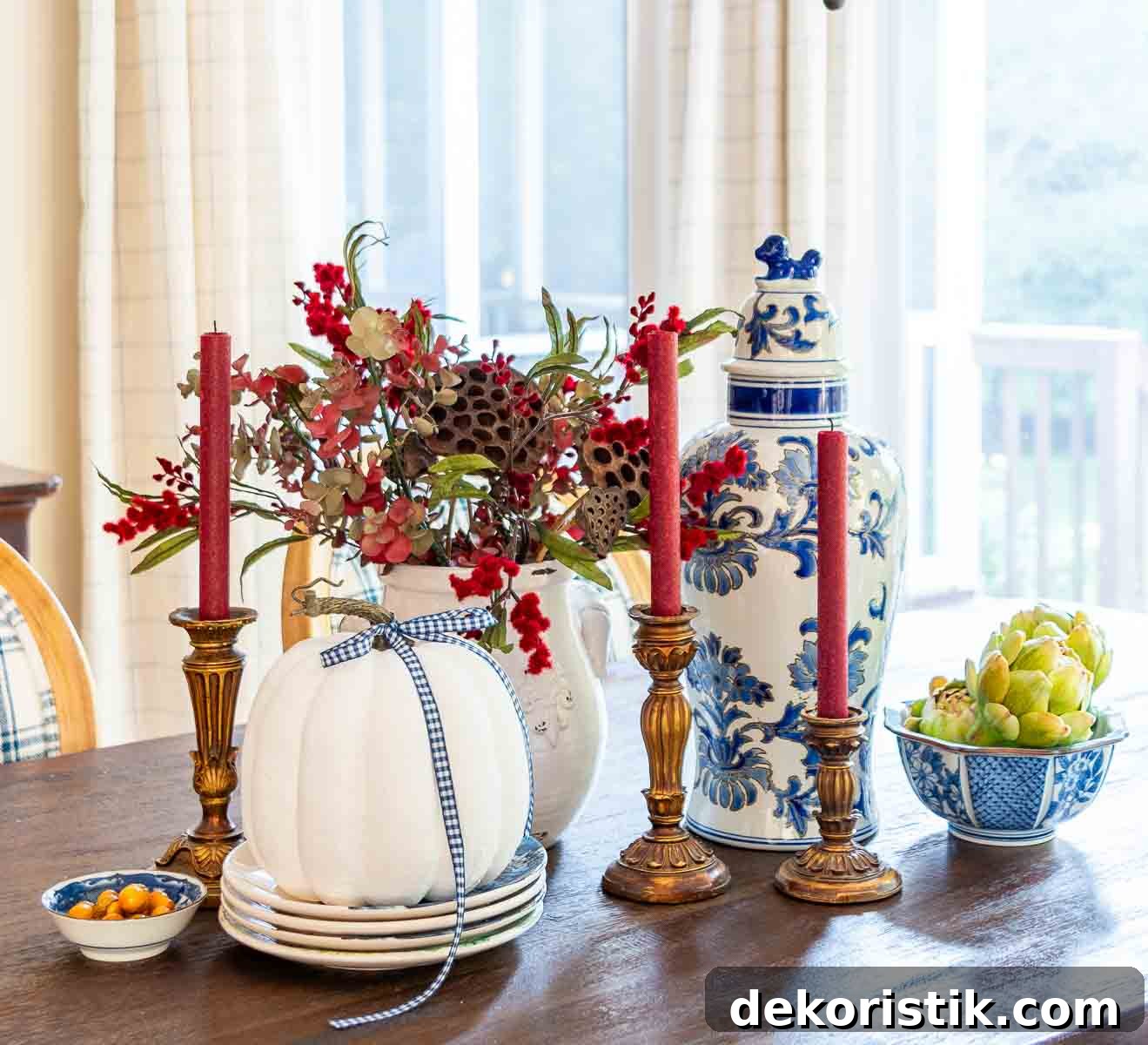 a diy fall table centerpiece using blue, white and burgundy colors, consisting of a large lidded urn, a floral arrangement, and a large white pumpkin on a stack of fall plates