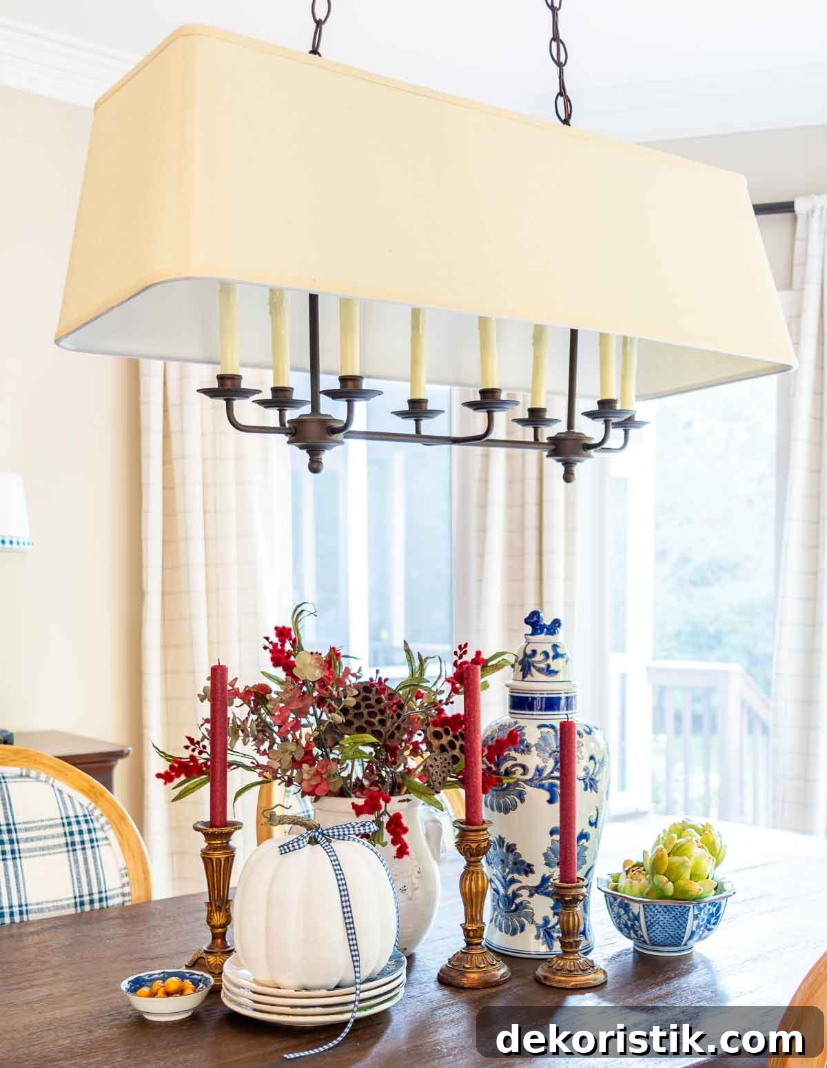a diy fall table centerpiece using blue, white and burgundy colors, consisting of a large lidded urn, a floral arrangement, and a large white pumpkin on a stack of fall plates