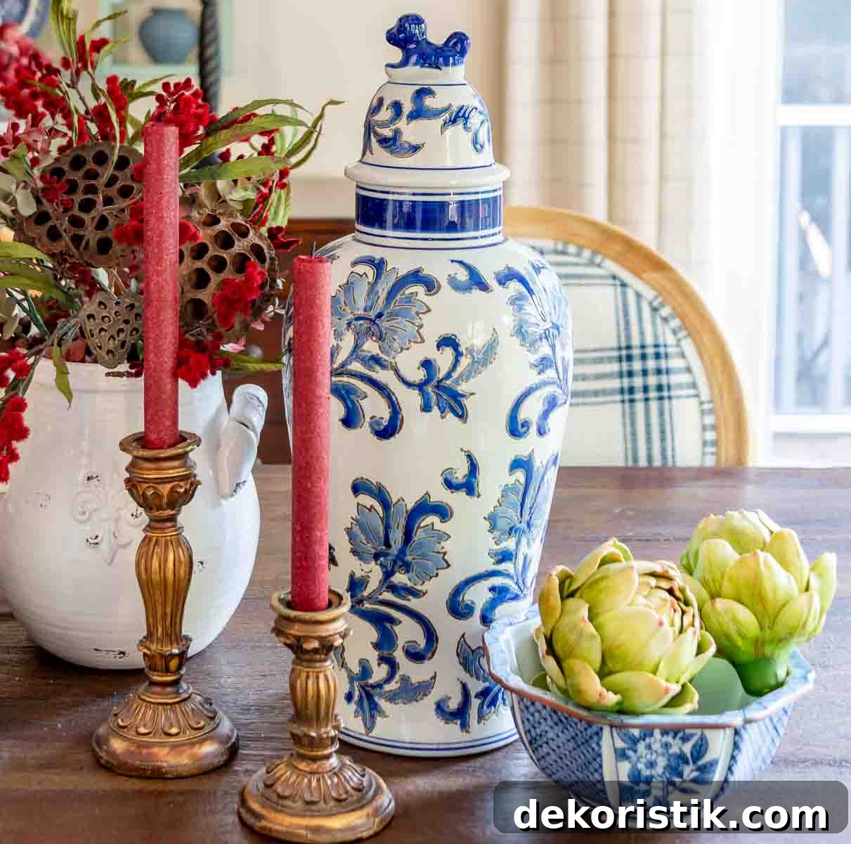 a diy fall table centerpiece using blue, white and burgundy colors, consisting of a large lidded urn, a floral arrangement, and a large white pumpkin on a stack of fall plates