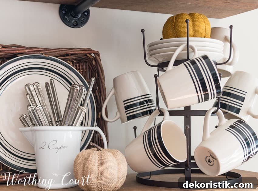 There is a orange fabric pumpkin on plates and a neutral fabric pumpkin beside the cups on the shelving unit.