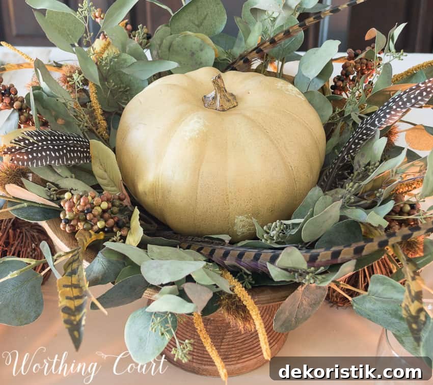 Thanksgiving centerpiece in a wooden pedestal bowl using a faux pumpkin, eucalyptus leaves and feathers || Worthing Court