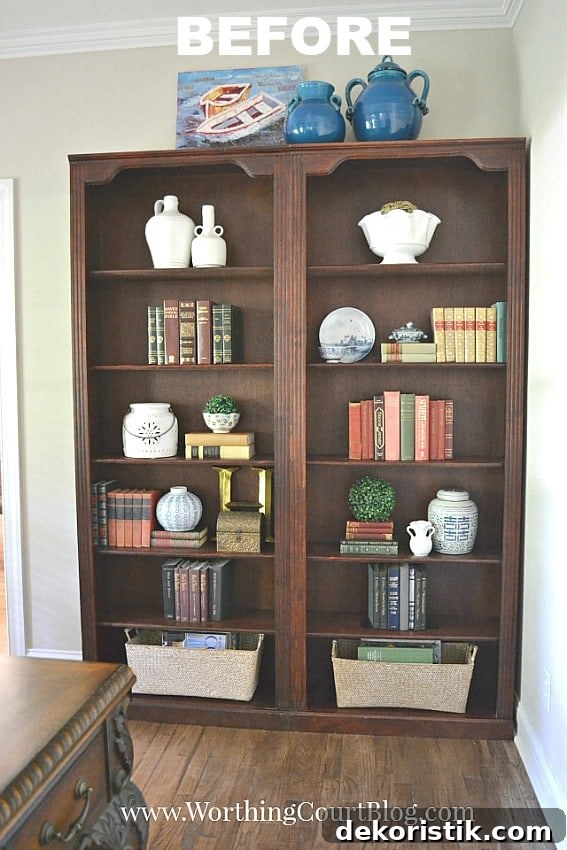 A traditional cherry bookcase in the office with books and pottery on it.