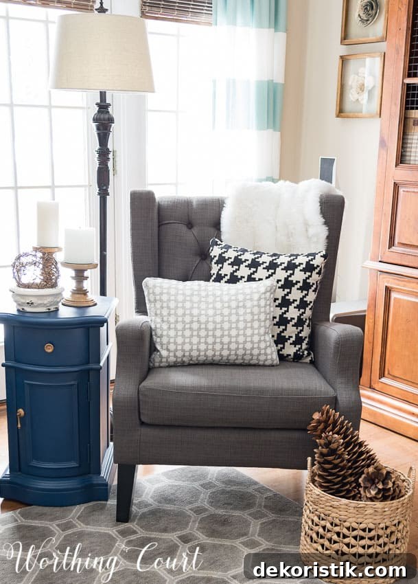 A gray armchair with throw pillows on it, and a woven basket full of pinecones.