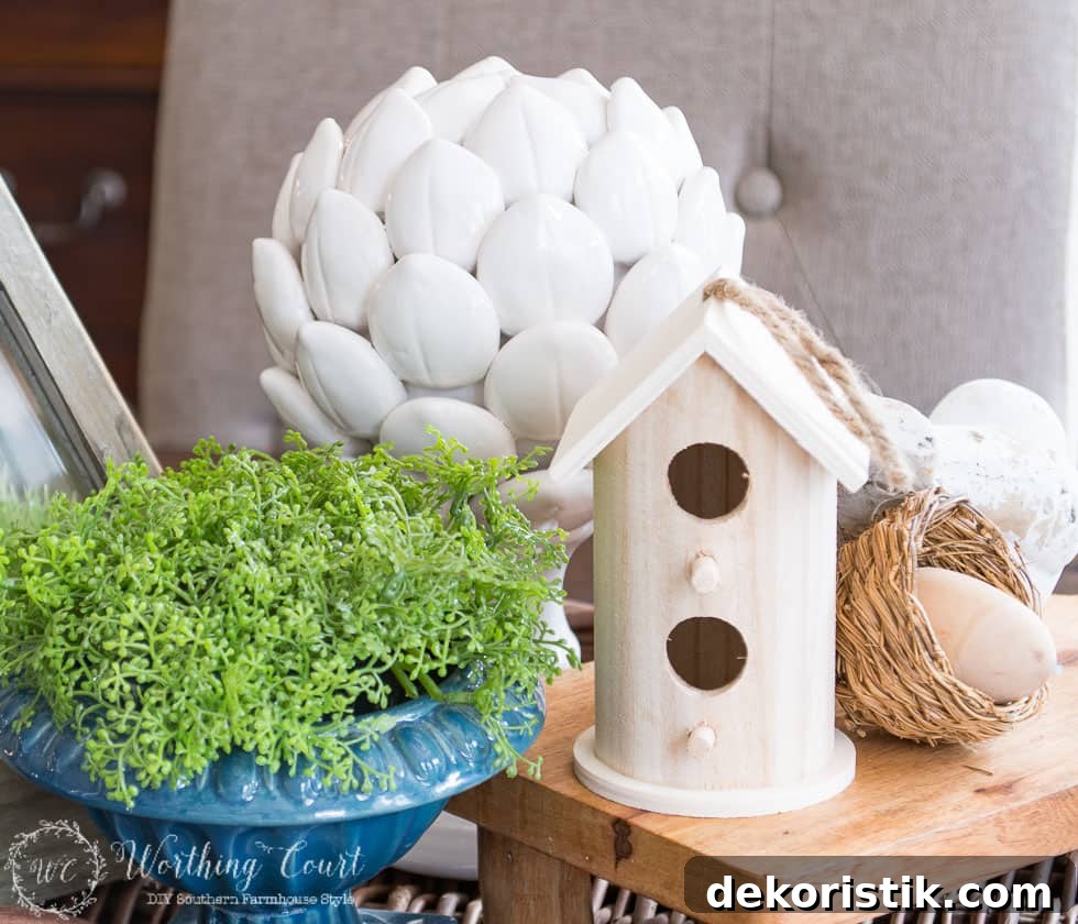A little wooden birdhouse beside a blue vase filled with greenery.
