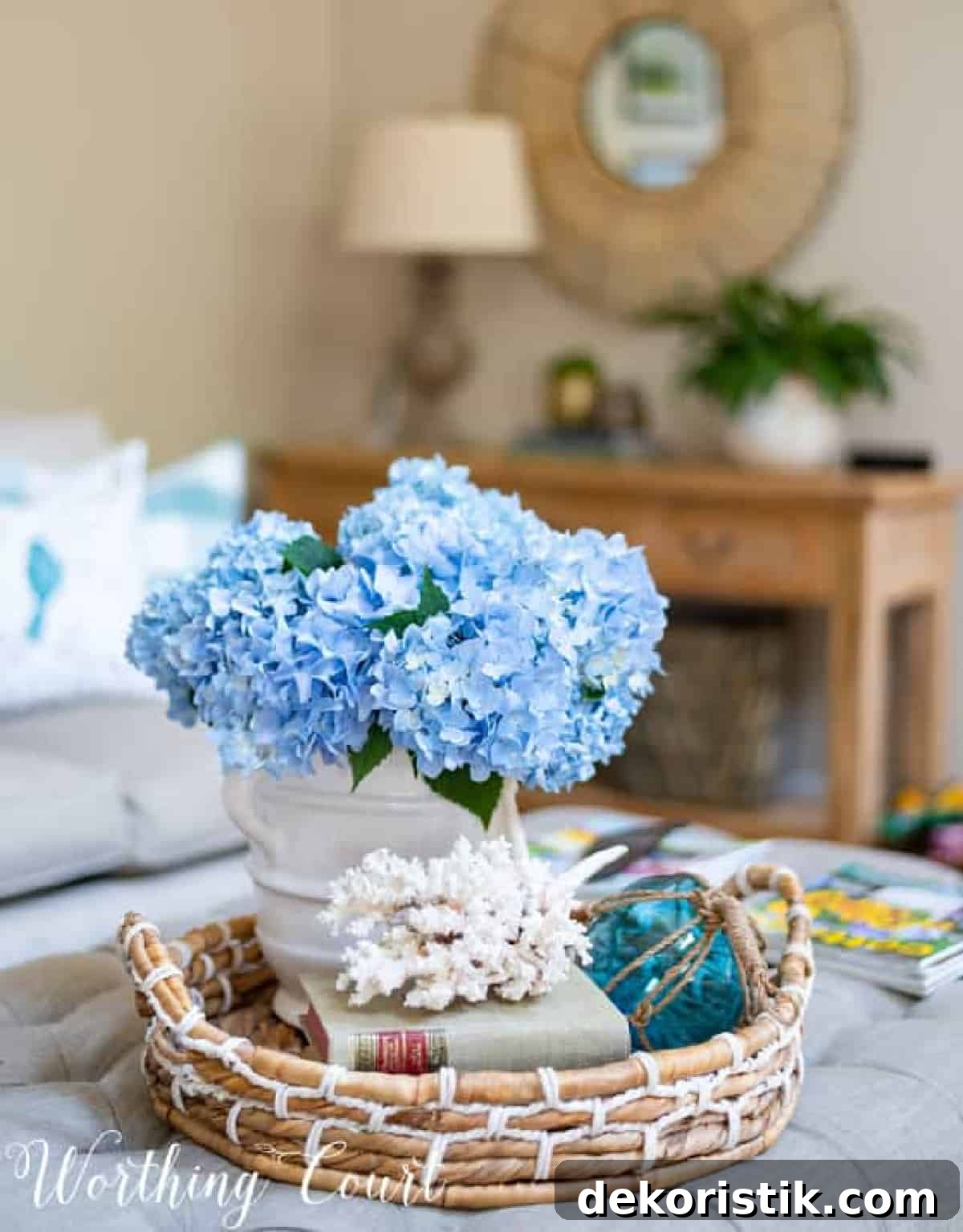 summer vignette with blue hydrangeas in a white vase with coral and a fishing float