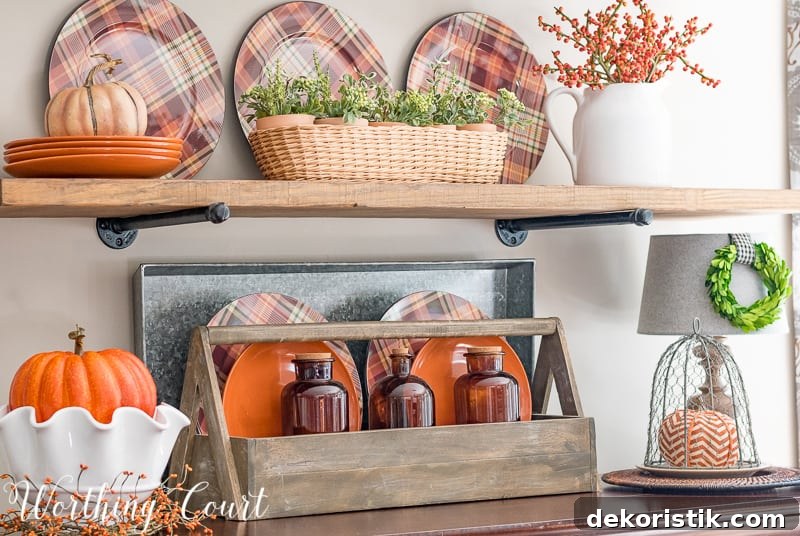 Fall shelf decorating ideas with plaid plates, brown glass bottles, pumpkins and a toolbox.