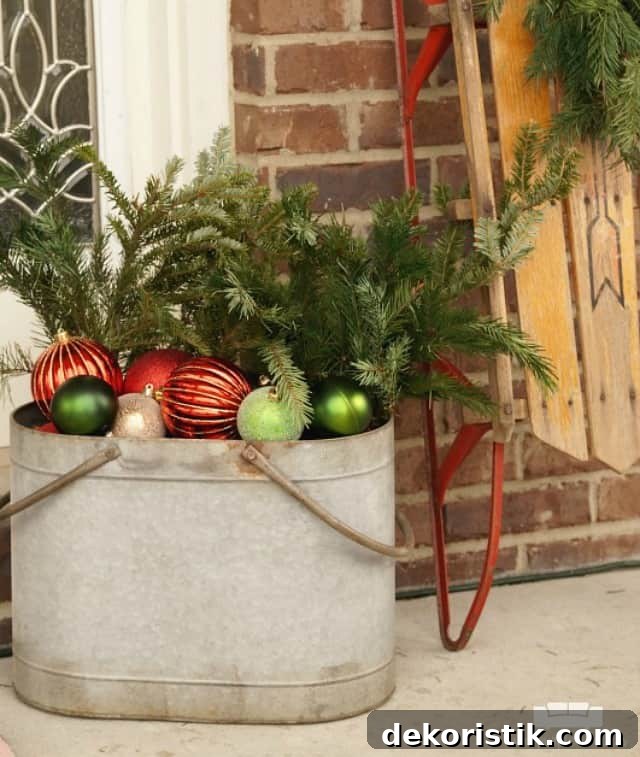 A galvanized bucket is filled with ornaments and evergreen branches on the porch.