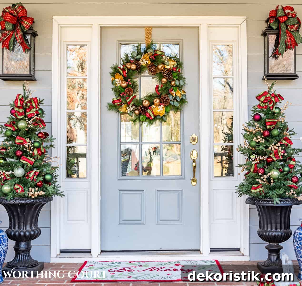 front door with a Christmas wreath flanked by urns with small trees with red, green and gold Christmas decorations on them