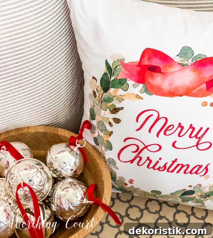 Merry Christmas pillow beside wood bowl filled with silver bells