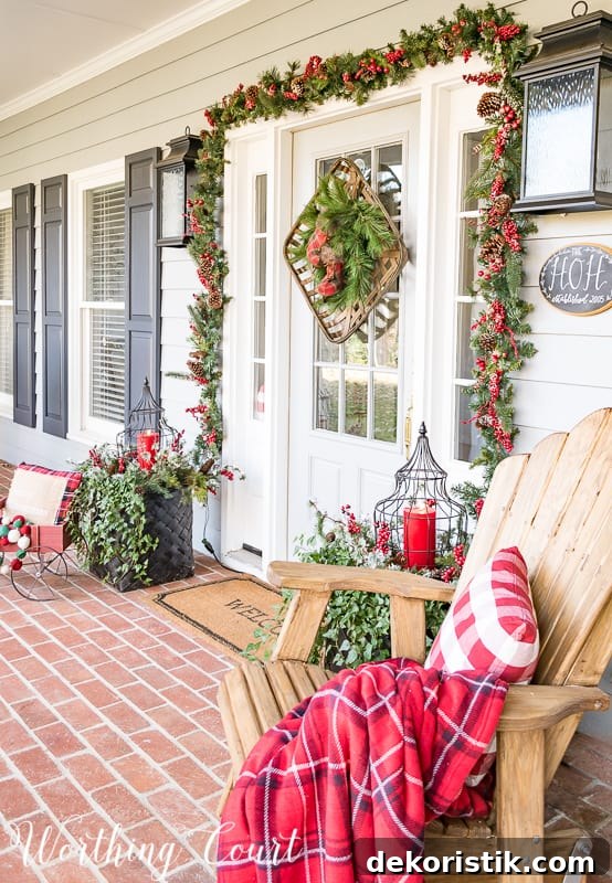 The front porch decorated with an adirondack chair with a red and white pillow and a throw blanket.