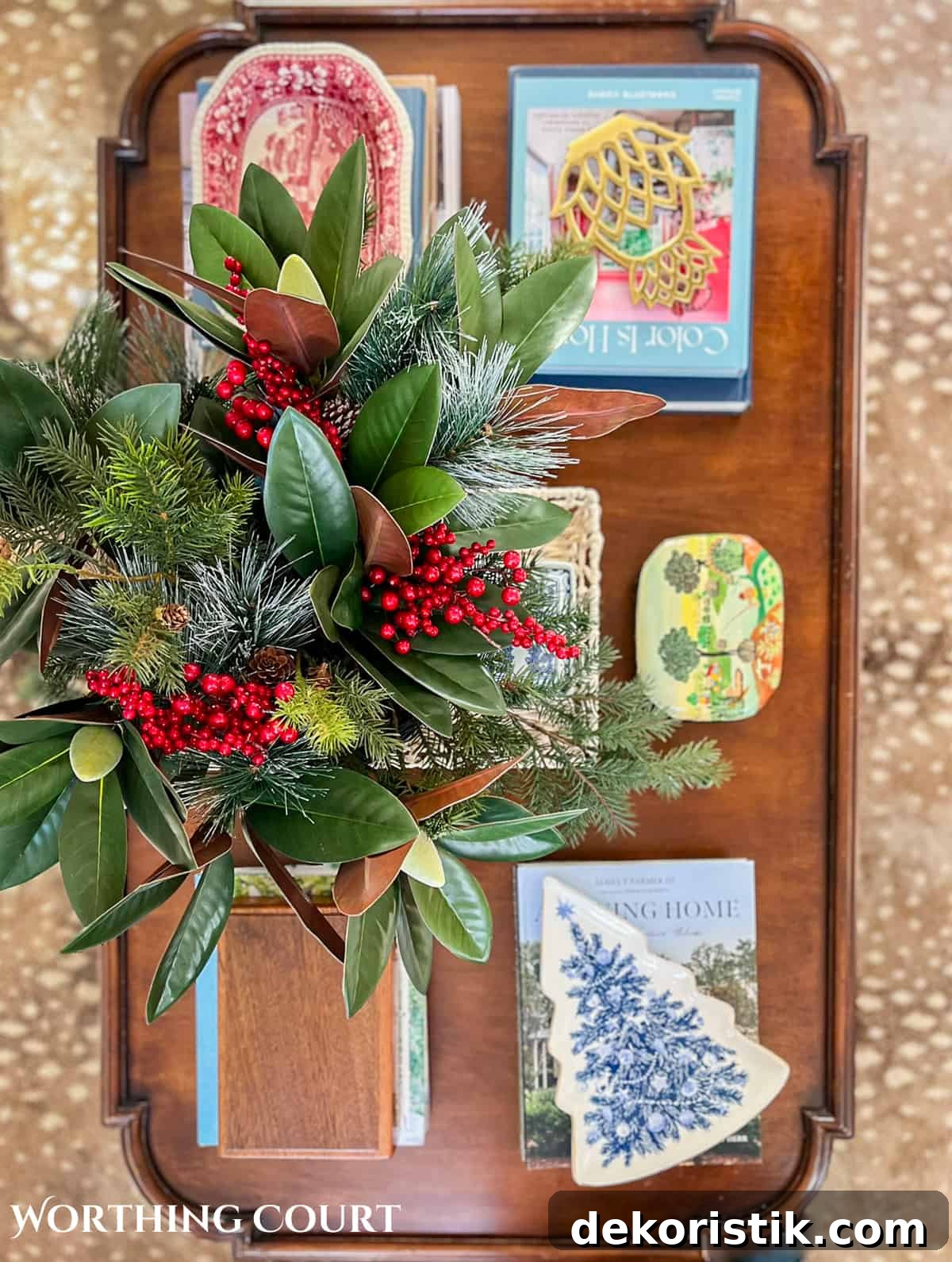 wood coffee table filled with easy decorations for Christmas consisting of coffee table books, Christmas dishes and a bowl filled with faux greenery and berries