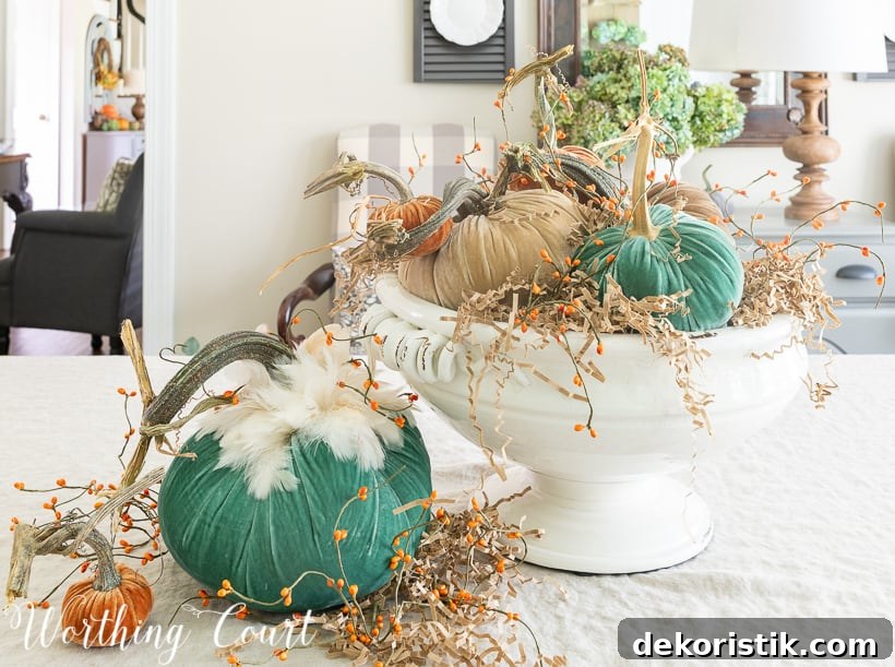 The velvet pumpkins are in a white ceramic bowl, with a large green and a small orange pumpkin beside it on the table.