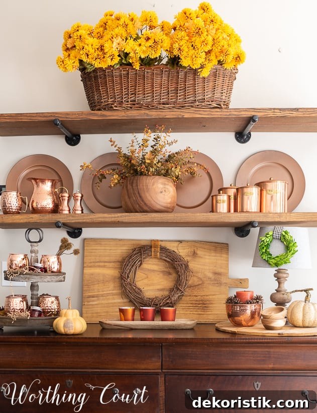 A large basket filled with Mum's, copper plates, copper cups and a wooden cutting board on the hutch.
