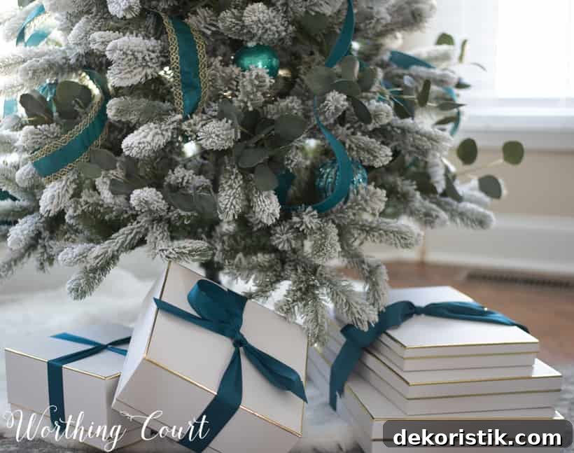 White gift boxes on a fur Christmas tree skirt with teal ribbons on the presents.