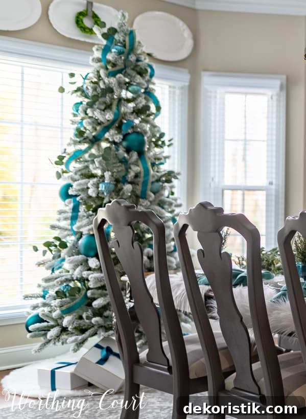 Flocked Christmas tree with teal decor and wrapped presents under the tree.