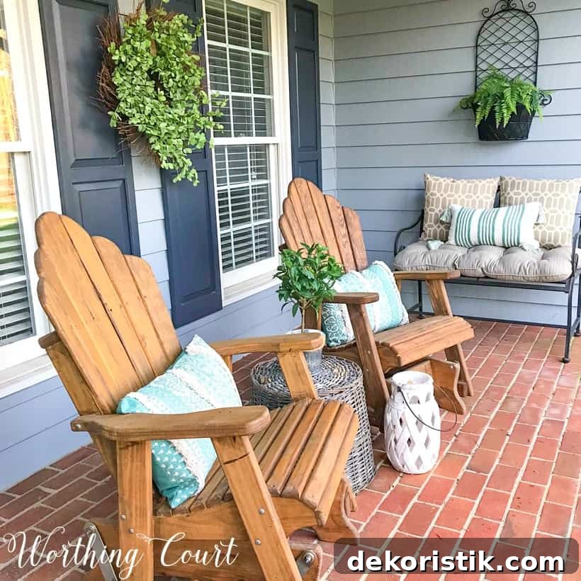 pair of wood stained adirondack chairs on a front porch with gray siding