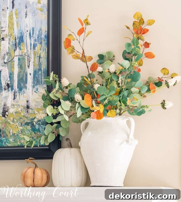 Faux fall eucalyptus stems in a white vase on a fireplace mantel.