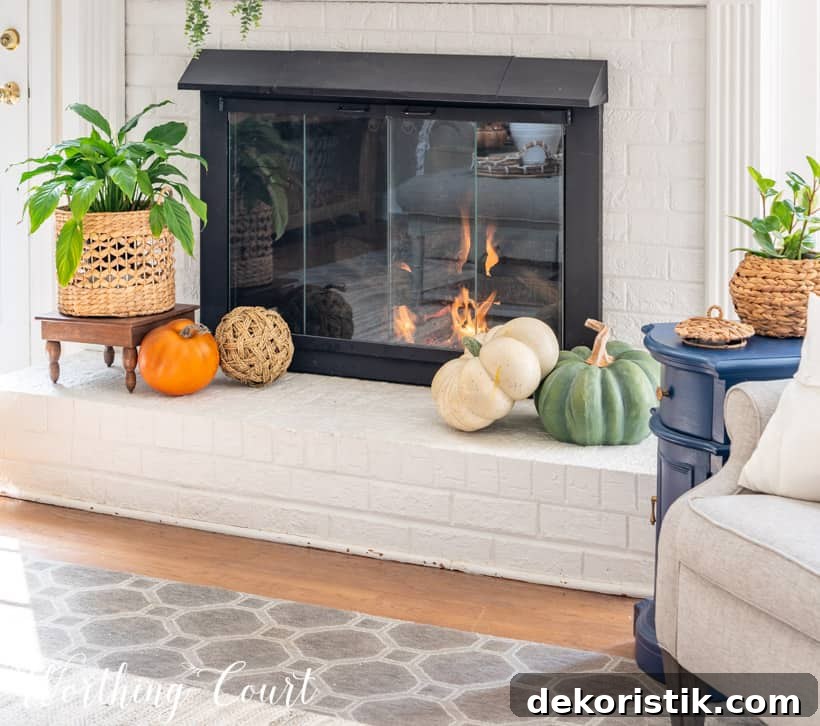 Fireplace hearth decorated for fall with faux pumpkins and an indoor plant.