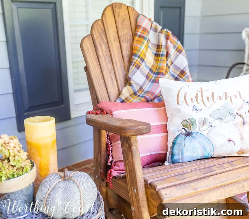 Front porch with fall decorations such as a pillow that says autumn, and pumpkins and candles.