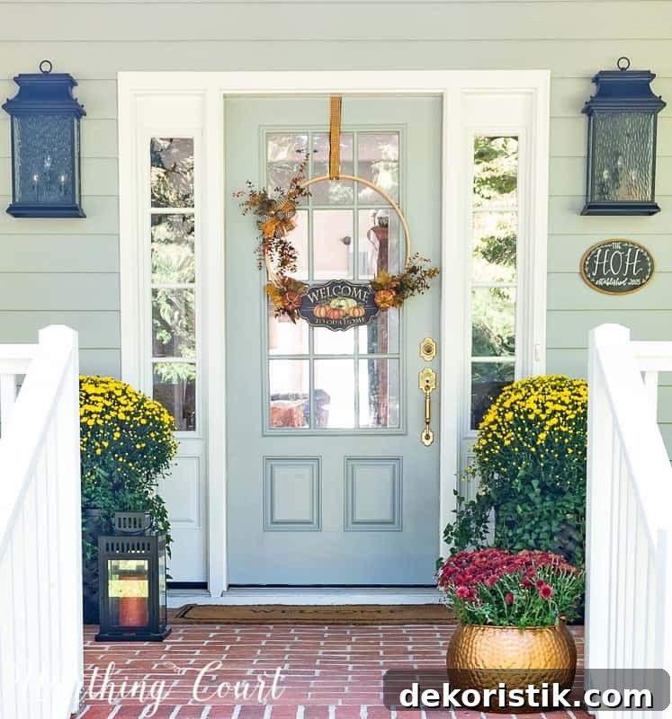 Front porch decorated for fall with mums and a Welcome sign on the door.