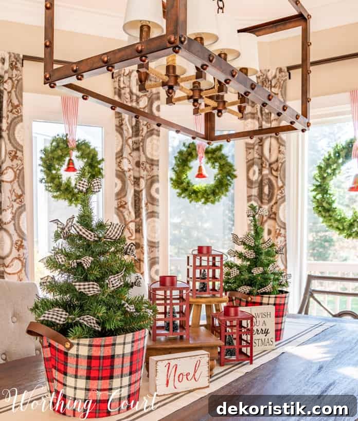 Christmas centerpiece with mini trees in plaid containers and red lanterns.