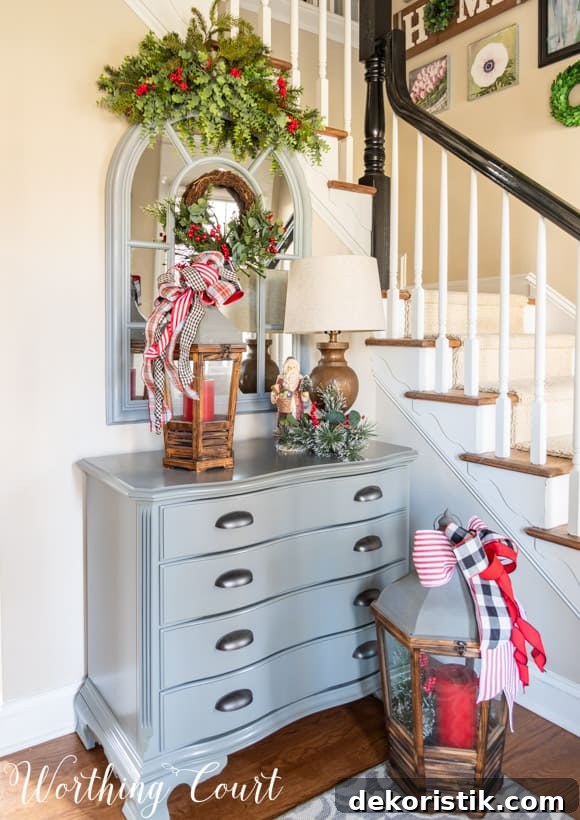 Small gray chest with an arched mirror above with a faux greenery swag and Christmas decorations.