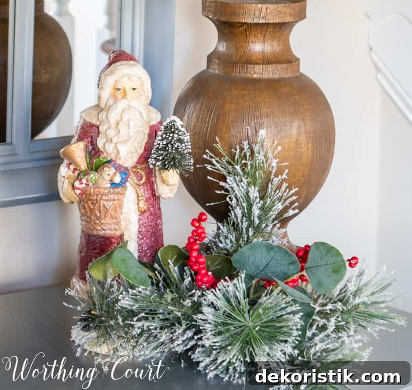 Christmas vignette with Santa figurine and faux greenery at the base of a lamp.