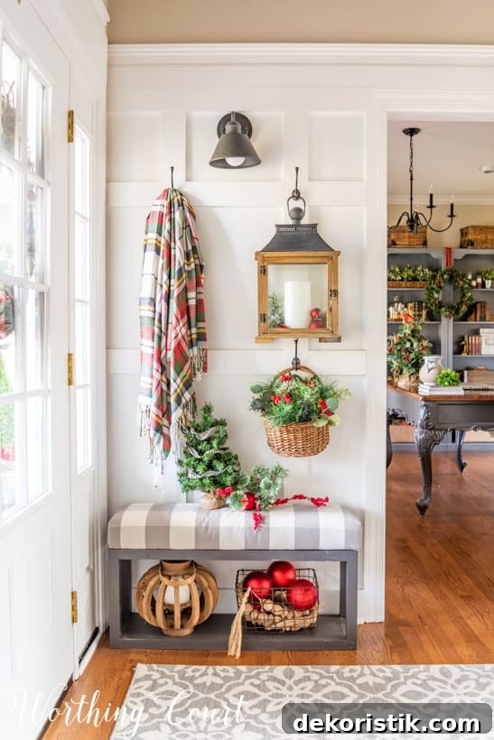 Board and batten wall with Christmas decorations hanging from hooks such as a plaid blanket and a small Christmas tree on the bench.