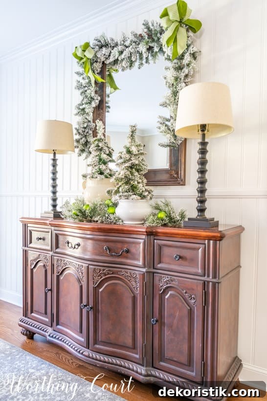 Sideboard with mirror above with flocked garland, flocked mini trees and green ribbon.