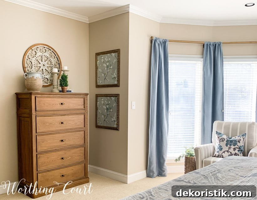 Master bedroom chest of drawers with blue draperies and framed wallpaper.