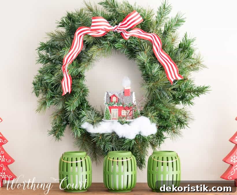 green Christmas wreath embellished with ribbon, fake snow and a tiny house
