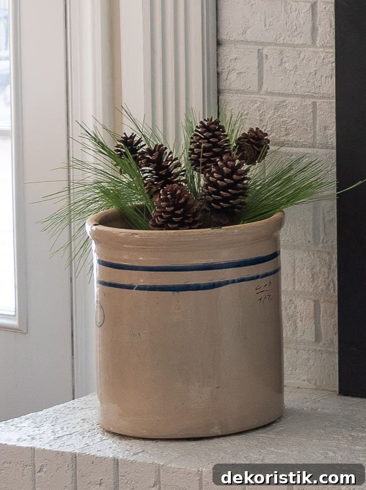 antique crock filled with faux pine greenery on a white fireplace hearth