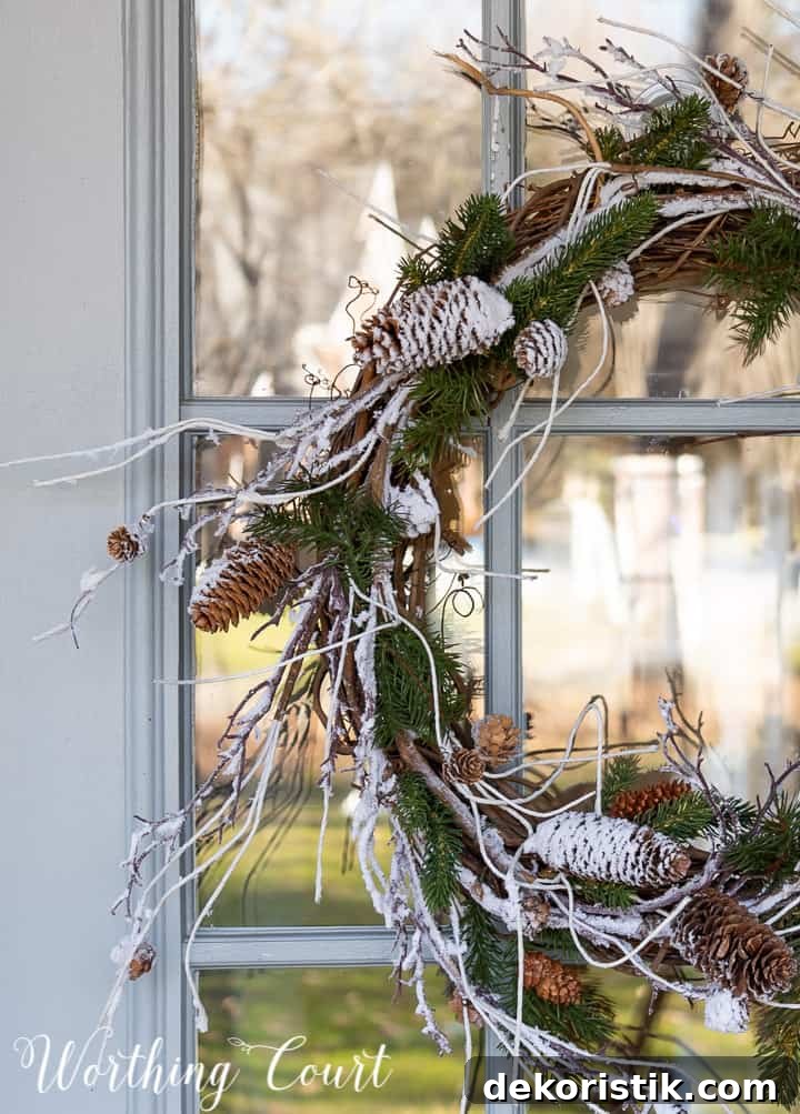 winter wreath with snow and pine branches and pinecones with a bow hanging on a glass door