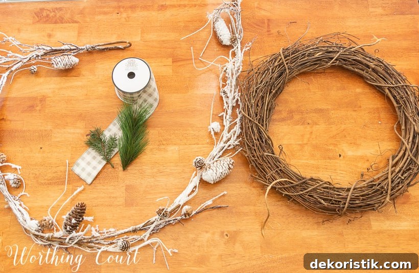 grapevine wreath, snowy garland, faux pine pieces and ribbon laying on a wood table