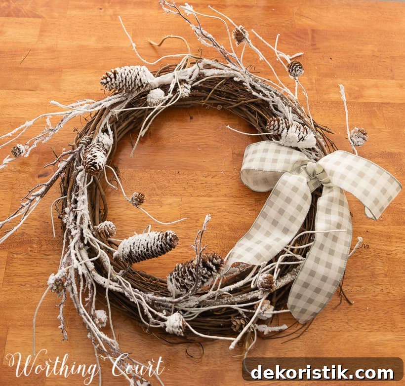 in process photo of the making of a wreath with snowy branches, pinecones and a bow