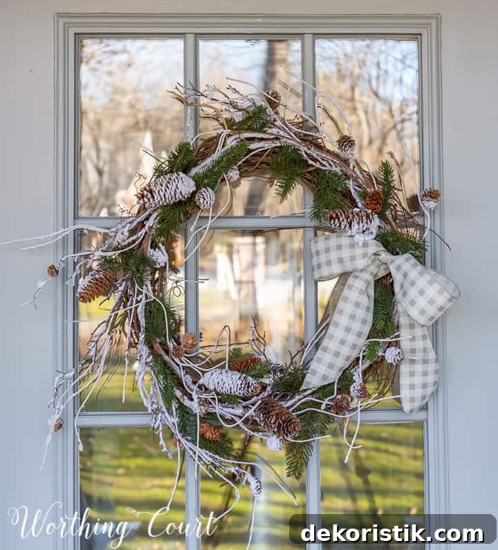 winter wreath with snow and pine branches and pinecones with a bow hanging on a glass door
