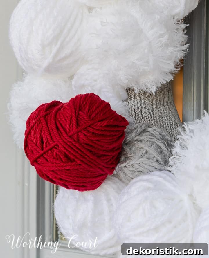Partial view of Valentine's Day wreath made with styrofoam balls covered with white and gray yarn and a heart cutout wrapped with red yarn