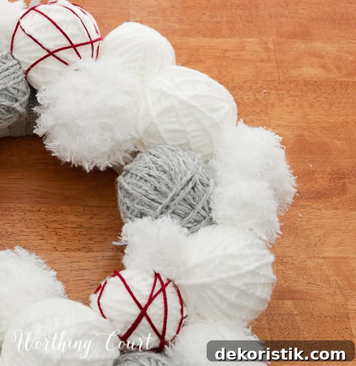 Partial view of Valentine's Day wreath made with styrofoam balls covered with white and gray yarn and a heart cutout wrapped with red yarn