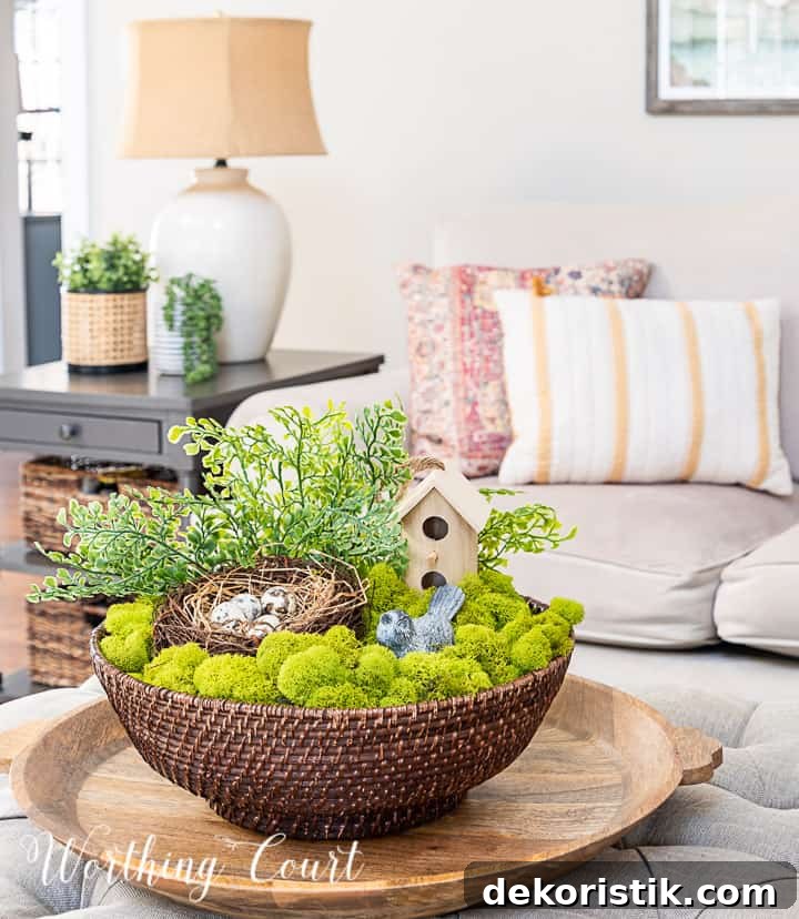 spring coffee table arrangement in a wicker bowl with moss, birdhouse, nest and greenery with couch in the background