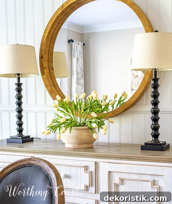 side board with round mirror above, two buffet lamps and white tulips in a wood bowl