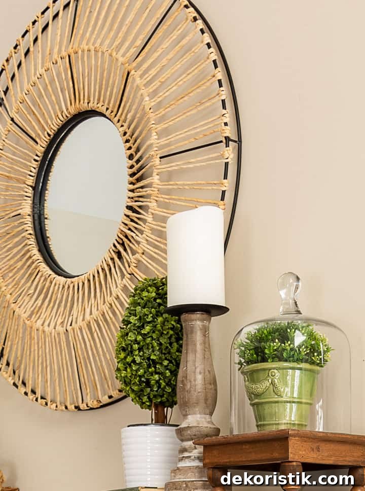 spring vignette with a topiary, candle and small plant under a glass cloche with a round mirror in the background