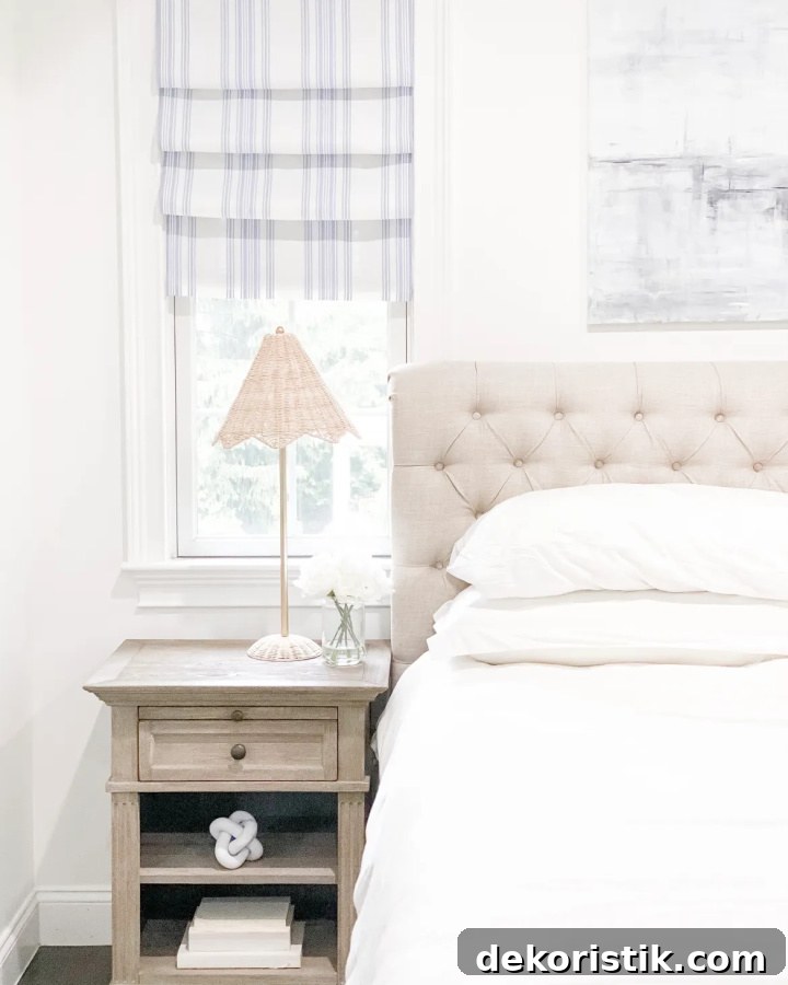 DIY Window Decor Ideas: Step-by-Step Tutorials 4 partial view of a bedroom with a beige upholstered headboard, white bedding, a beige night stand and a striped faux roman shade hanging in the window above it