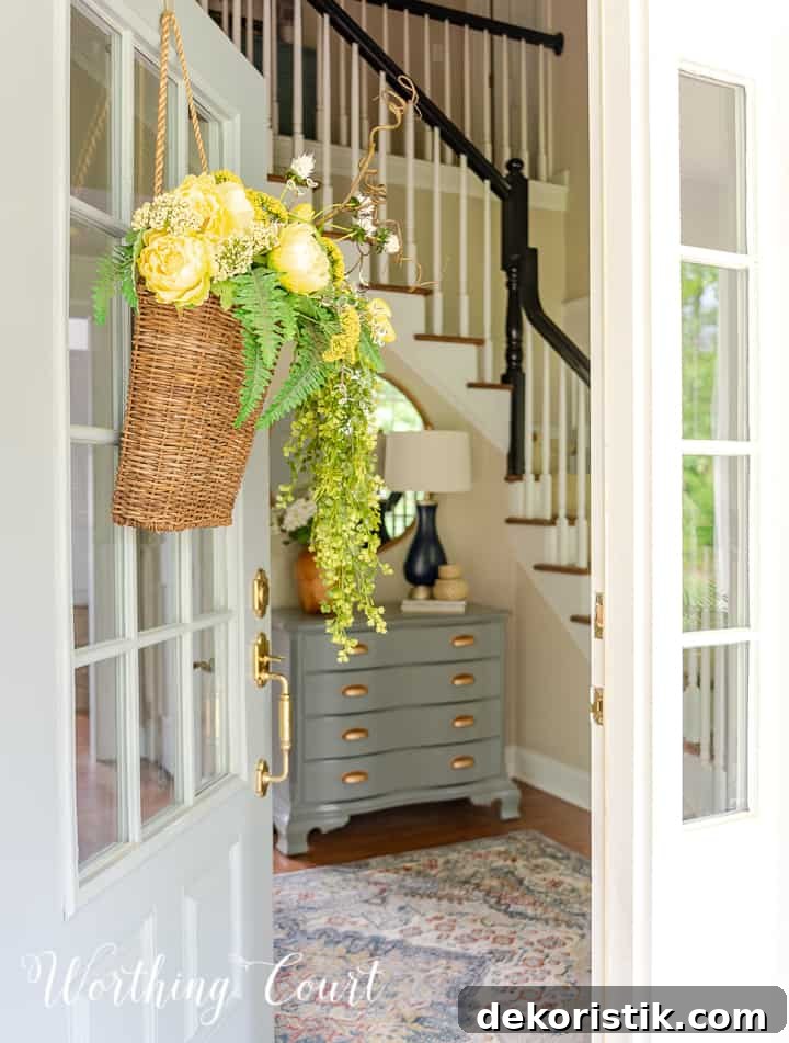 looking into a front door at a painted gray chest with gold handles and a round mirror